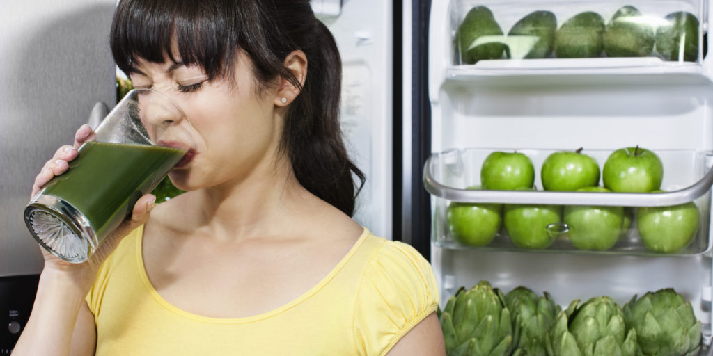 Girl frowning and drinking nasty green smoothie